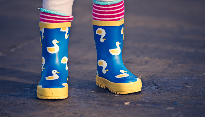 Close up of a childs feet wearing colourful wellies with ducks on them.